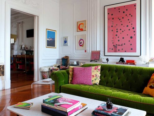 a living room, a green sofa, pink furnishings, amarela, a vibe/style of Mira Mikatti, a center of madeira, colorful objects of art, a wooden floor, a vibe of arte chic, classic and modern at the same time. natural light, and a white wall with molding and a white fabric.